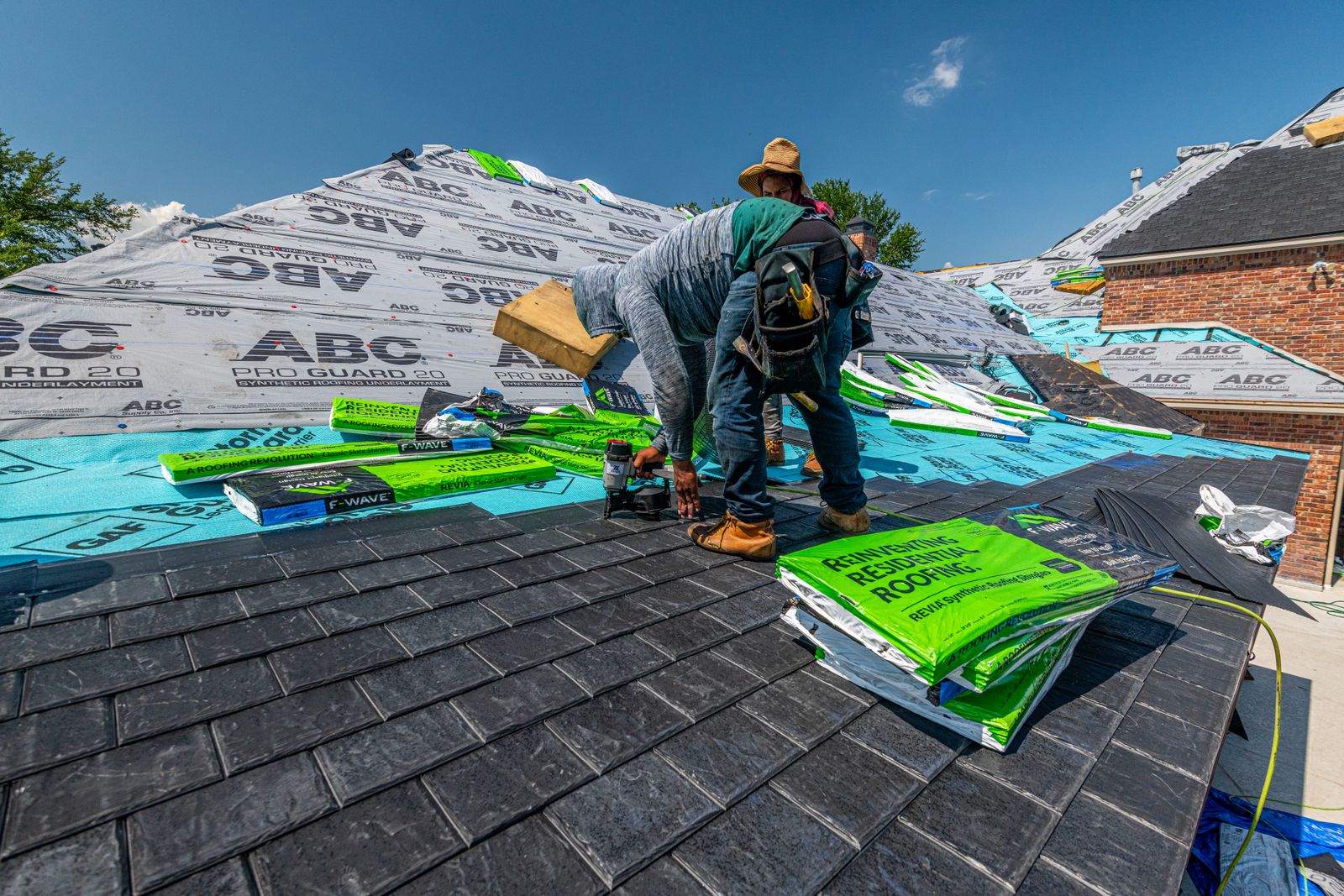 Roofers laying underlayment and shingles on a brick house